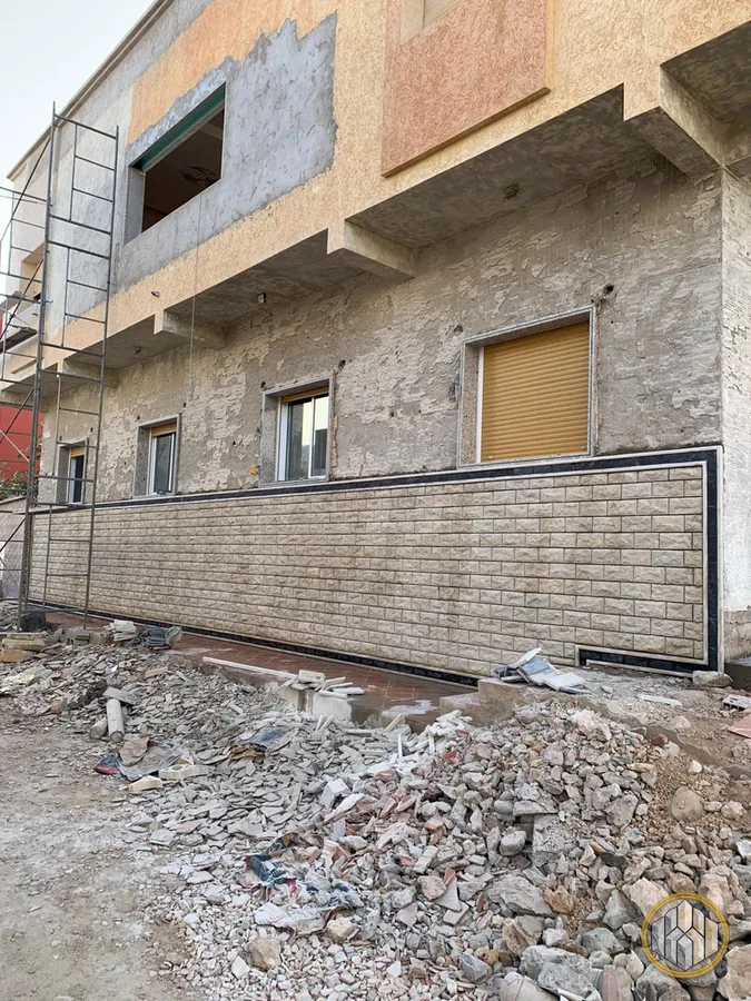 Soubassement en pierre posé en bas de façade, enduit brut encore visible au-dessus